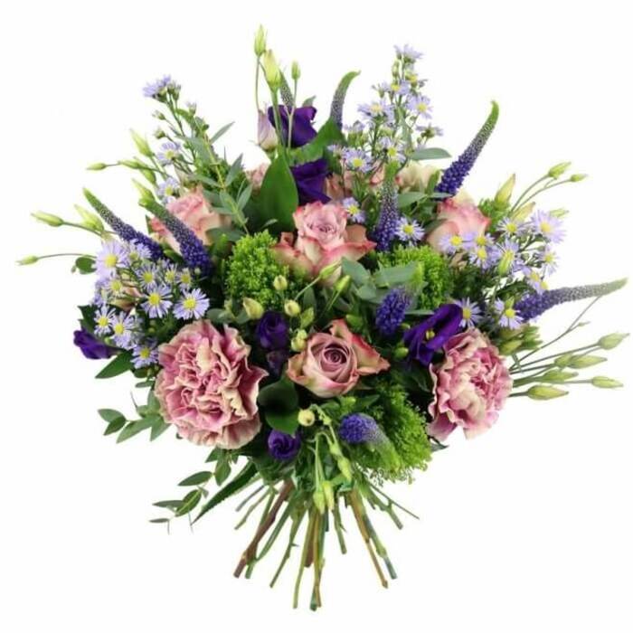 This image shows a beautifully crafted hand-tied bouquet, photographed against a pure white background to showcase its harmonious palette of pinks, mauves, purples, and lively greens. At the heart of the design are soft pink roses in various stages of bloom: some are still forming tight cups, while others have opened generously so that their concentric layers of petals move from a deeper rose-pink core to softer, almost cream-tinted edges. Supporting these are large, frilled carnations in dusty rose and muted purple-mauve, their many ruffled petals catching the light and giving the arrangement a rich, sumptuous texture. Rising through this gentle cushion of colour are refined spires of Veronica in deep lavender-blue, their narrow, tapering blooms adding vertical structure and a touch of modern elegance, reminiscent of the lines of new developments around Brent Cross and Hendon Way. Scattered among these taller stems are velvety, bell-shaped lisianthus blooms in a deep purple tone and small, cloud-like clusters of aster-like flowers in periwinkle and lavender-blue, each with a delicate yellow center that adds a subtle brightness. Encircling the flowers is an abundant mix of greenery: smooth, silvery-green eucalyptus leaves sit alongside other foliage in various shades of green, while vivid lime and chartreuse filler blooms punctuate the bouquet with bursts of freshness. The stems are gathered neatly at the base, cut to a uniform length and bound in the style of a traditional hand-tied bouquet, ready for a vase in a flat overlooking the junction or a family home off the North Circular. The arrangement conveys a feeling of thoughtful luxury and heartfelt sentiment, ideal for special occasions, from birthdays and anniversaries to just-because flower deliveries throughout Brent Cross and nearby neighbourhoods.