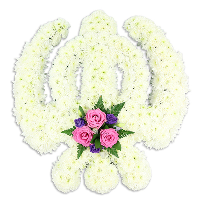 A reverent Sikh Khanda floral tribute is shown in close detail, floating against a clean white background that accentuates every curve and angle of the sacred emblem. The structure is completely covered with small, densely clustered white chrysanthemum florets, each bloom forming part of a continuous, plush surface that outlines the double-edged central sword, the circular chakkar, and the two sweeping kirpans. The petals create a soft, ruffled texture that invites touch, with subtle shadows falling into the recesses between the blooms. These natural variations keep the large expanse of white from feeling flat, instead giving the arrangement an almost sculptural character, as though the Khanda has been carved from living flowers. The base of the design holds a contrasting cluster of accent flowers, precisely placed where the kirpans cross. Three fresh pink roses, their petals spiralling in tight, velvety layers, take centre stage, suggesting tenderness and affection. Around them nestle deep purple blossoms with a more delicate structure, adding depth of colour and a quietly regal tone. Green fern fronds and small leaves frame the cluster, their darker hue grounding the composition. The overall effect is both solemn and comforting, perfectly suited to a Sikh funeral or memorial held for a Brent Cross family, perhaps remembered in a service near the North Circular or in the quieter residential streets that fan out from the shopping centre. The flowers hint at a gentle fragrance, a mix of crisp chrysanthemum freshness and the sweet, familiar scent of rose, offering a soft counterpoint to the weight of grief, and allowing the Khanda's message of faith, courage, and eternal remembrance to come through clearly.