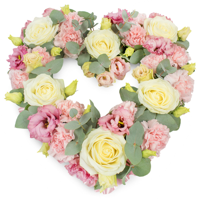 A beautifully detailed heart-shaped wreath is captured against a luminous white background, showcasing a blend of pastel blooms and greenery carefully composed for a funeral or memorial service. The heart is symmetrical and fully filled, the flowers placed so closely together that the arrangement looks dense and opulent, with no visible gaps. Cream and pale yellow roses serve as anchor points throughout the design, each one opening in a perfect spiral of smooth, velvety petals that suggest warmth, respect, and unconditional love. Between these roses, clusters of soft pink carnations provide contrast with their ruffled, almost frothy edges, giving the surface of the wreath a layered, textural richness. Deeper shades appear through magenta and mauve-pink lisianthus, their flared, cup-like blossoms and sometimes shadowed centres adding dimension and a quiet sense of depth, like the more complex memories we hold close. Silvery-green eucalyptus is threaded deftly among the blooms, its round and oval leaves following the curves of the heart, adding a cool, calming tone and a hint of fresh woodland fragrance. Small yellow-green buds are scattered discreetly throughout the composition, hinting at new growth and continuity even in the midst of mourning. The overall impression is serene and comforting, ideal for families in Brent Cross, Temple Fortune, or along the North Circular who are choosing flowers to mark a farewell. This heart wreath feels like a central tribute piece, whether placed near a casket, propped on a stand at a chapel, or delivered to a home gathering, offering a quiet but unmistakable expression of sympathy, love, and shared remembrance.