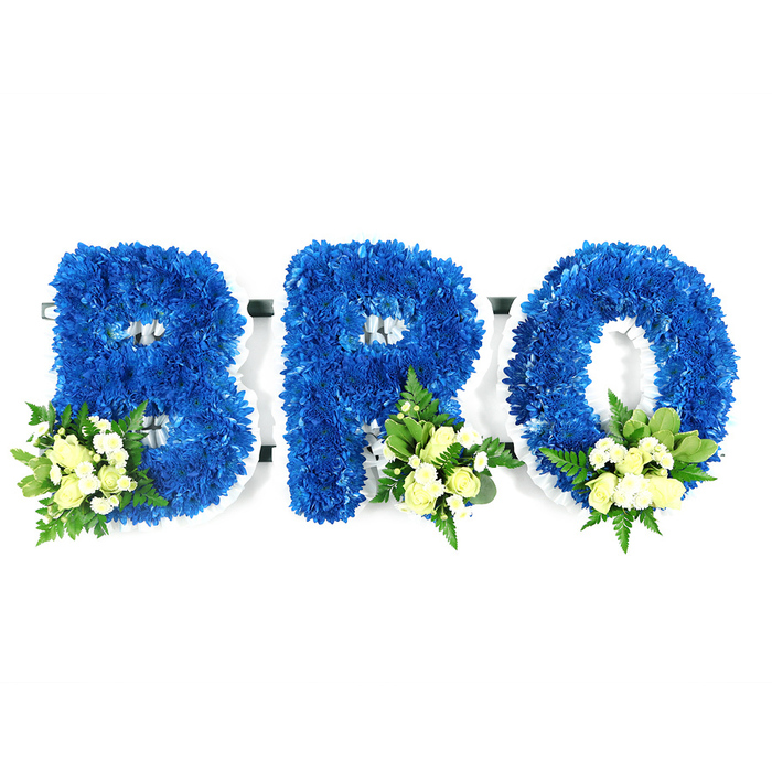 Displayed against a bright white background in a straightforward, dignified studio shot, three freestanding capital letters form BRO, each letter meticulously shaped from a dense mass of royal blue chrysanthemums that create a lush, velour-like surface of tiny florets. The craftsmanship is evident in the clean outlines and the thin white support frame-likely floral foam-visible around the edges and through the letter openings, which secures the blooms and maintains the composition's architectural precision. At the base of each letter, carefully positioned accent clusters introduce softness: the B carries a spray at its lower-left, while the R and O are adorned toward their lower-right sides. These accents pair creamy pale-yellow or ivory spray roses-some in tight bud and some slightly open-with small white filler flowers (mini chrysanthemums or delicate baby's breath) and a mix of green foliage, from broader glossy leaves like salal or lemon leaf to finer, fern-like fronds that add air and texture. The lighting is neutral to preserve the deep, saturated royal blue and to render the ivory tones with gentle warmth, reinforcing a mood of respectful remembrance. This three-piece sympathy tribute reads as a heartfelt address to a lost brother, a visual embrace of memory that families in Brent Cross, Cricklewood and Hendon might choose for a funeral service or graveside dedication. Prepared by Brent Cross Flowers, it combines traditional symbolism with meticulous studio presentation for a serene and personal memorial expression.