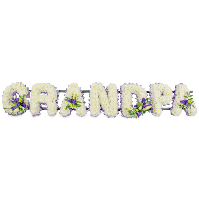 The photograph captures a poignant floral tribute in the form of the word GRANDPA, crafted from individual block letters and arranged in a straight line against a bright white background, much as it might appear when displayed at a funeral in Brent Cross. Every letter is fully blanketed with small, tufted white chrysanthemums or carnations, the heads sitting close together to create a seamless, richly textured surface. The flowers are arranged in a shallow dome, so the letters feel three-dimensional and sculptural, not flat cut-outs. Their pure white colour suggests innocence, remembrance, and the quiet dignity that often characterises a farewell for an elder loved one. Interspersed among the white petals are pockets of deep purple and soft lavender blooms, accompanied by small sprays of fresh green foliage that bring natural movement and life. These coloured accents are placed with intention: you can imagine seeing them nestled along the curve of the G, brightening the centre of the first A, adding depth to the vertical and curve of the D, then appearing again within the P and final A, guiding the eye gently from one end of the tribute to the other. A neat violet ribbon trims the edges of the letters, helping define their contours and adding a further ring of gentle colour. Underneath, a dark green support rail runs discreetly beneath the flowers, linking the letters into one cohesive piece that can be laid along a coffin top or propped on stands at a service in a local Brent Cross church or crematorium chapel. Overall, the design feels thoughtful and personal, ideal for Brent Cross families wishing to honour a grandfather's memory with flowers that balance tradition, simplicity, and heartfelt affection.