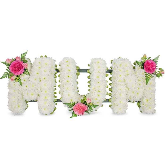 In this detailed funeral arrangement, the word MUM is artfully spelled out in stout, capital block letters, each one resting on a narrow dark green support bar that runs horizontally along the base. The letters themselves are densely filled with crisp white spray chrysanthemums, creating a uniform surface that looks soft yet substantial, like a carefully padded cushion. Each tiny blossom is tightly packed, their petals overlapping in gentle layers, and faint hints of pale green centres add subtle variation within the sea of white. The entire tribute is photographed against a plain white background, so the colours of the flowers and the careful craftsmanship stand out clearly, without distraction. To add warmth and a personal touch, the florist has placed three matching accents of coloured flowers and foliage. At the top left of the first M, a bold focal cluster of fuchsia garden roses and lighter pink spray roses blooms from the white base, their rounded heads and curling petals creating a rich, sumptuous contrast. Fine green fern fronds extend around them, softening the edges and bringing a sense of natural movement, reminiscent of greenery in parks and gardens around Brent Cross. The lower middle of the U holds a second, similar cluster that dips gently into the negative space between the letters, while the top right of the last M is capped by the third cluster, completing the visual journey across the word. The tribute feels quietly elegant and deeply affectionate, suitable for a funeral, memorial, or graveside visit for families in Brent Cross who wish to honour their mother with a traditional yet distinctive floral message of love and remembrance.