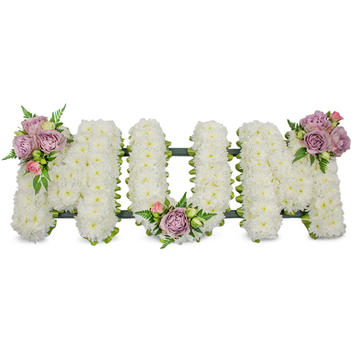 A large, heartfelt floral tribute spells MUM in bold capital letters, each letter densely covered with hundreds of pristine white chrysanthemums to create a uniformly soft, textured surface that reads as purity and calm. The bouquet is set against a clean white ground so the crisp whites glow and the small, tightly packed blooms show their delicate petal structure and slight variation in tone. Three artful accent clusters of soft lilac and pale pink roses are placed with careful symmetry: one on the upper left arm of the first M, another nestled in the low curve of the U, and the final group sitting on the upper right arm of the last M. Within each cluster some roses are open and fragrant, others remain as tender buds, and each is cushioned by vivid green leaves and slender fern-like foliage that introduce texture and depth. A darker green framework - either ribbon-wrapped support or moss-covered base - peeks out at the letters' edges, giving the arrangement a defined silhouette and reliable structure while remaining unobtrusive. The overall feeling is one of reverent grace, a traditional funeral tribute chosen to convey deep love and lasting remembrance for a mother. Prepared by Brent Cross Flowers with flowers often chosen fresh from local suppliers near Brent Cross Shopping Centre and the markets around Cricklewood, this standing tribute is intended for services, wakes or graveside dedications and radiates quiet comfort and skilled craftsmanship.