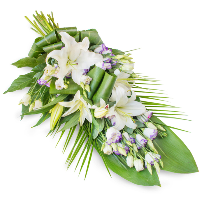 A refined, teardrop-shaped sympathy spray composed of white lilies and lisianthus is presented on a pure white background, allowing every curve and contour of the design to stand out clearly. The arrangement is fuller at the upper end, where the stems are secured, and gradually narrows to a delicate point, creating a sense of gentle downward movement. At its core, several prominent white oriental lilies command attention: some have fully opened, their star-like petals forming generous, almost sculptural blooms with soft green centres, while others remain in bud, slender and upright, hinting at flowers yet to unfold. Interlaced among the lilies, airy lisianthus blossoms in white add intricate layers, their petals often tinged at the edges with faint lavender or light purple, providing a whisper of colour that feels tender rather than bold. Small buds and partially opened lisianthus flowers are scattered thoughtfully throughout, giving a sense of natural growth and balance. The floral display rests on a bed of lush greenery; broad, glossy leaves form a dense, dark green backdrop, some carefully folded or rolled into contemporary, tubular shapes that rise close to the central blooms. Long, narrow palm-like fronds sweep out from one side and along the length of the spray, emphasizing the elongated silhouette and offering a flowing rhythm reminiscent of the steady traffic lines near Brent Cross and Hendon Way. The overall impression is one of understated luxury and respectful calm, as though the arrangement has just been prepared in the Brent Cross Flowers workshop and is ready for delivery to a local crematorium or family gathering. The cool whites and deep greens work together to evoke peace, remembrance, and the enduring cycle of life, making this spray a fitting choice for funerals, memorial services, and expressions of heartfelt condolence in the Brent Cross area.