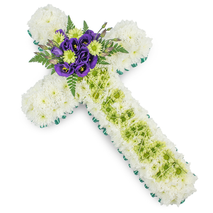 In this photograph, a sophisticated cross-shaped floral tribute is presented on a bright white background, allowing every element of the design to stand out clearly. The entire shape of the cross is padded with a thick covering of small white chrysanthemums, their numerous petals creating a uniform, plush texture that feels gentle and serene, like a hush over the busy roads around Brent Cross. Around the very edge, a slim band of vivid green ribbon or closely set foliage runs continuously, tracing the outline of the cross with a clear, contemporary edge. This precise border gives the arrangement a neat, tailored appearance, while the green hue adds freshness and a connection to the natural world. At the centre of the vertical arm, a channel of lime green button chrysanthemums runs from just below the focal point down toward the base. These rounded, button-like flowers create a lively yet controlled stripe of colour that breaks up the white surface. Draped over this green section, delicate pale green wires intersect in a subtle criss-cross pattern, forming an understated decorative mesh that suggests both craftsmanship and care. The focal point of the design is placed at the heart of the cross, where the arms intersect. Here, deep purple lisianthus blooms are clustered together, their velvety, gently ruffled petals arranged tightly to build a rich, jewel-like centre. Threaded among them are lime green blossoms that mirror the tones of the vertical stripe. Around this central cluster, dark green fern fronds and soft foliage extend outward, adding depth and a touch of airy movement. Created as a funeral or memorial tribute, this floral cross from Brent Cross Flowers expresses remembrance, respect, and quiet hope for families gathering in local churches and crematoria.