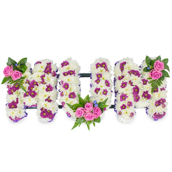 Presented on a clean white field, this handcrafted sympathy tribute spells 'MUM' in three substantial, sculpted letters that read at once like a message and a soft, tactile wreath. Each letter is densely layered with pristine white chrysanthemum blooms, their tiny petals creating a velvety, pillowed surface that suggests innocence and enduring affection. Interspersed within that white field are small, vivid patches of magenta or deep purple pom-pom chrysanthemums that add subtle rhythm and shadow, helping the letters retain depth from every angle. At carefully chosen points - the upper left of the first 'M', the lower inner curve of the central 'U', and the upper right of the last 'M' - groups of vibrant pink spray roses form warm focal bouquets. These roses are surrounded by lush fern fronds and varied dark green foliage which provide contrast and a natural frame, and delicate blue accent flowers offer tiny cool notes against the warmer tones. A discreet dark horizontal support runs behind the letters, visible only as a thin line that stabilises the composition while keeping the floral surfaces uninterrupted. The overall mood is tender and composed: a bespoke memorial piece that reads as both traditional and lovingly modern. A seasoned Brent Cross florist would note the careful balance between texture and colour here - how the whites soothe, the pinks console, and the magentas lend dignity - making this 'MUM' tribute appropriate for a funeral service, chapel display, or reflective home remembrance in and around Brent Cross and nearby Golders Green.