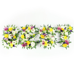 A clean, head-on view shows a horizontal floral lettering tribute spelling "BEST", each capital letter densely packed with freshly arranged flowers and edged with rich fern fronds against a pure white backdrop. The overall tone is bright and uplifting: cheerful yellow roses and gerbera daisies dominate alongside generous white chrysanthemums whose many petals create a soft, cloud-like texture. Interspersed through the composition are dusky lavender lisianthus and striking magenta spray roses or carnations that create lively, respectful accents. Tiny clusters of pale green and cream filler blooms nestle between the larger heads, creating gentle pockets of negative space that let the main flowers breathe while adding tactile depth. The fern leaves act as a dark, graceful frame for each letter, their lacy fronds curling slightly over the petals and lending the piece a natural, garden-fresh finish.

A subtle dark green or metal support bar is visible in places - notably within the horizontal arm of the E and near the base of the T - showing the structural care taken to keep the letters upright during procession or display. The photograph's bright, even lighting highlights the freshness of each bloom, the satin sheen on rose petals and the feathery texture of chrysanthemum disks. Scent, though unseen, is suggested: a gentle rose sweetness with a hint of green, comforting rather than overpowering. Thoughtfully composed, this floral word tribute balances dignity and celebration, a fitting choice for memorials or remembrance services, and a familiar piece created for families from Brent Cross through to nearby Cricklewood.