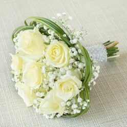 Emanating subtle sophistication, this bridal bouquet encapsulates the classic beauty and gentle warmth that have become hallmarks of Brent Cross celebrations. Set atop a softly textured light beige background, the bouquet brings together eight to ten creamy white and pale buttery roses, each opening in a quiet symphony of texture and tone. Wafts of delicate white baby's breath interlace the central roses, offering airy lightness and an almost lace-like intricacy that hints at the refined tastes found in the Brent Cross community. Bold yet graceful loops of slender seasonal greenery arc throughout, adding a touch of movement and framing the blooms in a way that feels at once structured and romantic. The stems are expertly wrapped in luminous silver ribbon, adorned with orderly rows of small, lustrous white pearls that invite a gentle caress. Below, the natural cut stems give a peek of garden freshness-a testament to the expert care invested by Brent Cross Flowers. Whether designed for a heartfelt wedding moment or as a cherished anniversary token, this bouquet quietly dazzles, reflecting the warmth and sophistication found throughout NW4 and its surrounding neighbourhoods.
