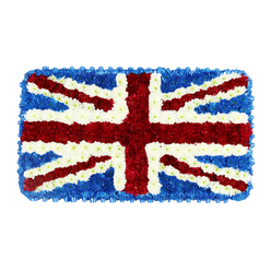 This image presents a carefully constructed floral Union Jack, arranged as a rectangular tribute that resembles a soft, blooming flag laid out to honour a life. Every inch of the design is covered with compact flower heads, creating a plush, cushion-like texture that visually softens the strong geometry of the British flag. The central St George's Cross is boldly expressed in rich red flowers, their densely layered petals forming solid bands that run vertically and horizontally across the middle, echoing the strength and steadiness of the design. Diagonal bands of red, suggesting St Patrick's Cross, cut across the flag with equal precision, each edged with slim stripes of clean white blossoms, which maintain the correct separation between colours. These white flowers fan outward into the broader diagonal arms of St Andrew's Cross, providing luminous contrast against the deeper shades. Around these elements, a close-packed field of royal blue blooms fills the remaining triangular spaces and forms a neat border, lending the arrangement a strong frame and intensifying the patriotic palette. The tribute is photographed against a simple white background, which allows the intricate detail of each petal and the subtle variations in tone to stand out clearly. From a distance, the piece reads as a flawless Union Jack; up close, you can almost imagine the faint, fresh scent of the flowers used. This floral flag is designed as a dignified funeral or remembrance tribute for families around Brent Cross, from those who gather near Brent Cross Shopping Centre to communities along the A41, offering a heartfelt way to celebrate a loved one's British identity and connection to North West London.