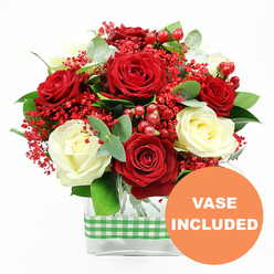 In this image, a striking bouquet of red and white roses is presented against a bright white backdrop, its colours and forms showcased with gallery-like clarity that feels at home in the stylish residences around Brent Cross. The focal point is a generous gathering of deep red roses and creamy ivory roses, each bloom open and plush, with petals that layer and fold into sumptuous spirals. The rich reds provide intensity and warmth, while the pale roses glow softly, bringing contrast and a sense of calm elegance. Threaded delicately between these larger flowers are airy clusters of tiny, bright red filler blooms, similar to dyed gypsophila, which create a fine, lace-like veil of colour that softens the overall silhouette. Nestled among the petals, rounded red hypericum berries gleam with a lacquered shine, introducing a subtle three-dimensional rhythm and a joyful, festive note that would suit special dinners or celebrations near Hendon and Cricklewood. The bouquet is framed by fresh greenery, including cool-toned eucalyptus and other leaves in various shapes, whose elongated forms and muted greens offer a sophisticated counterpoint to the saturated reds and creamy whites. All of this floral artistry is gathered neatly into a clear rectangular glass vase, through which the stems are visible-cut cleanly and arranged with professional precision. Around the middle of the vase, a green and white gingham ribbon is wrapped, its soft pattern introducing a rustic, kitchen-table charm that balances the bouquet's elegance. In the bottom right corner of the composition, an orange circular emblem with bold white text reads "VASE INCLUDED," making it clear that this arrangement arrives complete and ready to place on a coffee table, dining surface, or reception desk as a romantic surprise, anniversary gift, or simply a thoughtful floral delivery within the Brent Cross area.