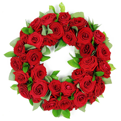 Across Brent Cross and the surrounding NW4 corridor, a circular wreath of red roses rests against a pristine white backdrop, a quiet testament to craft and care. Dozens of velvety blooms are packed into a generous ring, each rose at a slightly different stage of opening, from tightly furled buds to softly opened faces that catch the studio light and glow with warmth. The colour range runs from ruby to burgundy, a living spectrum that seems to inhale and exhale with the viewer's gaze. Intertwined among the roses are sprigs of fresh green foliage: broad, matte eucalyptus-like leaves that soften the edge of the red tide, and slender, glossy ruscus that provide a crisp, architectural heartbeat to the arrangement. The textures are rich and tactile-the satin sheen of each petal, the springy resilience of the stems, the gentle rustle of the foliage as a breeze might brush through a window. The wreath is a circle without seam, a universal symbol of remembrance and continuity, rendered here with a refined opulence that never overwhelms. Light falls softly from above, casting delicate highlights across overlapping petals and turning the greens into a velvet frame for the crimson core. This piece communicates sympathy, honor, and enduring connection, making it a natural choice for funerals, memorial services, or anniversaries of remembrance in Brent Cross and nearby communities. For those writing about floral tributes or memorial displays, this wreath offers a clear, tangible example of traditional symbolism-red roses for love and remembrance, green foliage for growth and renewal-beautifully realized by a local florist with decades of experience in the area.