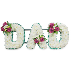 This solemn floral lettering forms the name DAD in bold capital letters, each letter built from a compact mass of immaculate white chrysanthemums that create a soft, pillowy texture across the whole design. A vivid emerald-green ribbon, pleated and ruffled, traces the outer and inner edges of each character, providing a crisp graphic edge that contrasts with the flowers' gentle curves. Behind the letters a discreet dark green or grey support rail links the three letters and gives the piece a quiet, stable presence for display on a stand or at a graveside. Accents of deep magenta roses - some tightly furled, some partially open - are grouped with small sprays of white freesia and deep green foliage to add depth and a living quality. The placement is deliberate: a cluster on the upper left curve of the first D, another cradled in the A's lower V, and a matching cluster on the upper right of the closing D, creating visual symmetry and a human touch. The overall scent is a soft mingling of rose and freesia, while the chrysanthemum base gives a clean, peaceful visual. Photographed against white, the composition reads with dignity and restraint, ideal for funeral services, memorial tributes, or a chapel display. As a piece frequently requested in NW London, it's an expression of comfort and respect often arranged for services in and around Cricklewood, Dollis Hill, and the wider Brent Cross community.