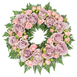 This image captures a thoughtfully designed sympathy wreath from a top-down perspective, displayed on a clear white background so the flowers and foliage stand out with calm clarity. The wreath forms a complete, even circle, built upon a generous layer of dark green fern fronds. These ferns, with their finely divided leaves and slightly glossy surfaces, create a textured, natural frame that peeks out between the flowers and defines the outer edge of the design. Above this lush greenery, large roses in refined tones of dusty lavender, soft mauve, and muted, grey-lilac purple are arranged with measured balance. Each bloom is fully open, showing concentric rings of velvety petals that curl gently at their tips, suggesting softness and serenity. Threaded among these focal roses are clusters of blush-pink spray roses and rosebuds, some tightly furled, others just starting to reveal delicate petals. Their lighter, warmer pink hue softens the overall palette and introduces an intimate, comforting feeling. Discreet accents of darker filler foliage and tiny buds are tucked among the roses, pulling the eye into the depths of the arrangement. The lighting is diffuse and even, giving the impression of natural daylight filtering into a studio near Hendon Way or the Brent Cross interchange, with no harsh contrasts to disturb the peaceful mood. This wreath would sit gracefully beside a coffin, memorial photograph, or book of condolence, offering a floral expression of sympathy for families in Brent Cross and neighbouring areas, conveying respect, remembrance, and a soothing sense of calm at a time of loss.