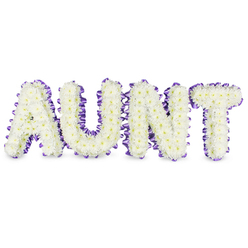 Taken from the viewpoint of a florist arranging a bespoke memorial piece, this image presents the letters 'AUNT' constructed from hundreds of small, immaculate white spray chrysanthemums, their layered petals forming a soft, tactile surface against a pristine white backdrop. Tiny pale yellow centres peek through several blooms, lending a quiet glow and natural detail to each letter. A rich purple satin ribbon outlines the perimeter of every character; the ribbon is pleated and gently ruffled as it follows the frames, its satin sheen catching subtle highlights and creating an elegant halo around the white blossoms. Fine grey shadows beneath the letters reveal the composition's depth and three-dimensional presence, as if the tribute were already ready to be placed on an easel at a service. The scent evoked is fresh and green, lightly dewy, a reassuring background to the visual calm. This is a design that favours tender dignity over mournful severity - white for purity and purple for remembrance - and reads as a celebration of a life remembered with affection. As a Brent Cross-based florist I think of delivering such a piece to local families near Brent Cross tube and the North Circular, or assembling it for service at nearby chapels in Cricklewood and Golders Green, where the careful construction and lasting choice of spray chrysanthemums bring comfort and respectful presence.