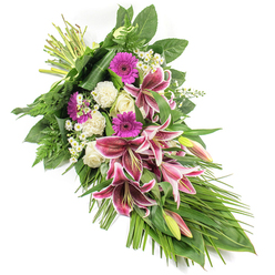 This refined sympathy spray is photographed against a pure white background, allowing its colours and details to stand out with clarity, much like seeing it laid out in a tranquil chapel near Brent Cross. The design stretches diagonally from top left to bottom right, forming a soft teardrop shape that suggests a gentle bow of the head in respect. At the heart of the arrangement sit several striking Stargazer lilies, their broad petals glowing in rich fuchsia-pink with crisp white edging and dark, wine-coloured speckles, some blossoms fully open, others still held in elongated buds tinged with green and pink. These lilies bring a sense of depth and solemn beauty. Interspersed among them are bright magenta gerbera daisies, their neat, round centres and layered petals offering a touch of warmth and cherished memory. Creamy white roses, in stages from tight buds to partially open blooms, cluster nearby, speaking of purity, honour, and heartfelt condolences. Nestled between these are ruffled white carnations, adding soft volume and an almost cloud-like comfort to the composition. Tiny white daisy-like filler flowers peep through, creating delicate points of light and innocence. Surrounding all of this is a rich mantle of greenery: broad, glossy leaves provide a solid foundation, feathery fern fronds introduce airy texture, and long, narrow leaves arc gracefully outward and downward, reinforcing the elongated, flowing form. The stems are neatly bound at the upper left, clearly showing the care and precision of a local florist, such as the team at Brent Cross Flowers, who understands the needs of families from Golders Green to Cricklewood. This arrangement carries a calm, respectful presence, perfectly suited for funerals, crematorium services, or memorial gatherings in the Brent Cross area.
