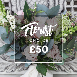 There is a slow, confident rhythm to this hand-tied bouquet: blush pink roses with petal-soft faces sit at the heart, encircled by dusty blue-green eucalyptus leaves that cool and ground the palette. Bright white berries-likely snowberries-dot the arrangement like small, luminous beads, lifting the composition and catching the soft afternoon light. Tiny sprays of white filler, suggestive of waxflower or astrantia, weave through the stems and create a delicate, wild-garden feel, while slender green-and-white spikes at the edges introduce a graceful vertical line that suggests snapdragons or similar spires. Deeper pink and burgundy accents are tucked into the middle layers to add shadow and richness, enhancing the sense of depth when the bouquet is viewed from any angle. The stems are tied in a careful hand-tie and bound with a cream-coloured satin ribbon that speaks to bespoke finishing; the tactile contrast between the velvet roses and the crisp, slightly prickle of the greens is immediate. The bouquet sits against a softly blurred, pale carved stone backdrop that hints at an elegant interior, and the whole scene is illuminated by soft, ambient daylight so the colours read natural and fresh. Curated by an experienced Brent Cross florist, this arrangement would be chosen for quiet celebrations-an anniversary at a nearby Brent Cross restaurant, a heartfelt thank-you delivered across the local neighbourhood, or simply to bring seasonal freshness into a home close to the reservoir. Brent Cross Flowers prepares bouquets like this with an eye for texture, scent and local delivery timing, ensuring blooms arrive just as fragrant as they look.