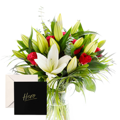 Elegance distilled into a single vase, this bouquet from a Brent Cross florist captures a moment of quiet heroism in the heart of Brent Cross. The white lilies stand at the core, their large trumpet blooms open with a calm, creamy gleam, while red roses thread through the arrangement with bold, romantic rhythm. A lattice of green fan and slender, glossy leaves runs between the blossoms, giving structure and lightness at once. The petals' satin textures invite a touch, the fragrance a refined veil of sweetness and spice that rises with every breath. Unopened buds hint at a continuing story of beauty to come, an invitation to celebrate what's ahead. A simple wrap frames the stems, and a small 'Hero' card nestled among them signals gratitude and admiration for someone who has shown courage and grace. This composition is designed to be both a personal gesture and a public tribute. It suits anniversaries, thank-you moments, or any occasion calling for heartfelt acknowledgment of strength. The overall mood remains generous and serene, never ostentatious, with the lilies and roses bathed in bright, clear light that makes each leaf and petal feel fresh and tangible. For deliveries across NW4, Golders Green, Hendon, Cricklewood, and surrounding streets, the same-day option ensures it arrives fresh and fragrant, just as pictured. Crafted by a local team who knows the area's corners - from the bustle of the Brent Cross Shopping Centre to the tranquil edges of Golders Hill Park - the arrangement embodies balance: courage with tenderness, celebration with gratitude.