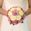 This bridal bouquet captures an elegant harmony of creamy white and blush-pink roses, arranged in a gentle dome that would rest beautifully in the hands of a bride crossing through Brent Cross's busy streets towards a calm wedding venue. The roses are tightly clustered, with each bloom opening into layers of soft, velvety petals that move from warm ivory to delicate pink and into touches of soft magenta. This subtle shift in tone gives the bouquet a painterly quality, like a softly blended watercolour held against the bride's gown. Threaded between the larger flowers are tiny sprays of white baby's breath, their miniature blossoms adding a fine, lace-like detail that softens the outlines of the roses and brings a feeling of airiness to the otherwise lush composition. Small accents of fresh green leaves emerge around the base and at the edges, giving the design a hint of natural movement and echoing the foliage you might see along local pathways and gardens. The bouquet's shape is rounded and symmetrical, carefully crafted so it appears balanced from every angle, exuding grace and serenity. Imagine brushing your fingertips lightly over the blooms, feeling the cool, satiny texture of the petals and inhaling a faint, sweet fragrance that suggests springtime around Brent Cross. Created by local florists who understand both tradition and modern romance, this bouquet feels like a promise held close-ideal for brides who want their flowers to whisper, rather than shout, their joy as they walk down the aisle.