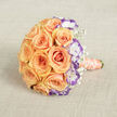 Captured from a slightly elevated viewpoint on a pale beige, textured fabric that resembles burlap or linen, this elegant bridal bouquet presents a lush, rounded silhouette that feels both intimate and expertly crafted. The heart of the composition is a dense cluster of full-bloom roses in soft peach and warm orange tones; each rose unfolds in concentric petals that appear almost tactile under soft, ambient light. Intermingled with the roses are white lisianthus whose petals are delicately edged in a striking deep violet, their ruffled margins bringing a cool, contemporary edge to the otherwise warm, sunlit palette. Wisps of white baby's breath nestle into crevices between larger blooms, introducing a light, cloud-like airiness that lifts the composition. The stems are wrapped in a light peach coral satin ribbon extending toward the lower right, and a strand of cream pearls coils tastefully around the handle, adding a refined, heirloom quality. The textured fabric beneath adds contrast and a handcrafted sensibility, as if the bouquet had been prepared in a Brent Cross studio before being entrusted to a bride setting off for photos at nearby Brent Reservoir or a reception by Cricklewood's leafy lanes. Subtle shadow and highlight model each bloom's volume and surface-the velvet of the roses, the crepe softness of the lisianthus, the fragile crispness of gypsophila-conveying scent, touch, and an overall mood of romantic celebration suited to weddings, anniversaries, or intimate vow renewals.