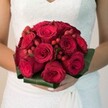 A Brent Cross bride is caught in a soft, luminous moment, her hands gracefully supporting a bouquet that pulses with romance and local meaning. At its core, plush red roses unfurl their petals in rich, velvety layers, exuding the classic beauty prized by generations of couples tying the knot near Brent Reservoir. Intertwined among these lush blooms, clusters of lively red hypericum berries bring a festive charm-bright as the joyful mood of local celebrations. A collar of smooth, emerald-green leaves surrounds the bouquet, lending shape and structure reminiscent of North West London's wide, leafy avenues. The bride's simple, elegant manicure and the delicate lace of her white dress highlight the arrangement's importance, while the gentle, ambient light casts a loving glow over the scene. Created by local experts for same-day delivery across Brent Cross, this bouquet captures the excitement of wedding mornings and the enduring promise of new beginnings-making it the perfect floral companion for those marking life's milestones in the heart of Brent.
