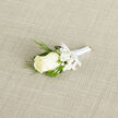 Laid with deliberate diagonal care across a subtle light-beige woven cloth, this boutonniere reads as an exercise in refined restraint and floral expertise. A single pristine ivory rosebud anchors the arrangement, its compact, creamy petals curling inward like a quiet embrace. Around that focal bloom, tiny clusters of white gypsophila create a soft, cloud-like halo, their miniature flowers lending air and lightness to the composition. Interspersed are slim, feathery sprigs of deep green foliage-evocative of cedar or evergreen-that introduce a darker, textural silhouette, their fine needles providing movement and elegance. Beneath these, broader, glossy deep-green leaves form a structural canvas, enhancing the rose's pale tones and ensuring the boutonniere reads clearly from a lapel.

The stems are carefully bound in a narrow white satin ribbon, tied in a small bow that keeps the piece tidy and wearable; the ribbon's satin sheen catches morning light in the way a well-placed detail should at a wedding or formal event. The neutral, natural-fibre background amplifies these contrasts, allowing one to notice the softer, powdery scent of the rose juxtaposed with the green freshness of the foliage. Imagining this piece being pinned on a groom or an honored guest in Brent Cross-perhaps after a quiet ceremony near the shopping centre or a photograph by Clitterhouse Playing Fields-invites a sense of place. It is a boutonniere that reads as both time-honoured and personal, made with the calm, considered touch of a florist who understands how subtle textures and tones carry meaning on an important day.