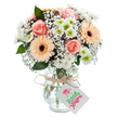 Bright and welcoming as an afternoon in Brent Cross, this bouquet is masterfully arranged to lift spirits and mark special moments. At its centre bloom lush, soft peach-pink roses, their subtle fragrance and velvety feel suggesting comfort and affectionate wishes. Two lively gerbera daisies, in soft orange and peach tones with deep brown hearts, flank the roses, projecting friendly cheer. Filling the spaces are airy sprays of white baby's breath and petite, white daisy-like chrysanthemums- each one showing off a fresh green eye and adding a layer of clarity and softness. Wisps of eucalyptus leaves pop through for texture and a faint herbal note. The arrangement rests in a clear, subtly patterned glass vase, the visible green stems and cool water highlighting its freshness and careful preparation. A rustic tie of raffia or natural twine circles the vase's neck, holding a simple white tag open for a message of joy, gratitude, or celebration. Altogether, this bouquet radiates warmth, expertise, and the distinctive charm of Brent Cross-a floral invitation to connect with loved ones and brighten the day.