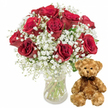 In this softly lit studio image, a timeless expression of affection is captured with clarity and warmth, reflecting the kind of romantic gifts often prepared for delivery in Brent Cross. On the left, a simple yet elegant clear glass vase stands upright, its sides perfectly transparent so that the bundled green stems inside are easy to see. The water in the vase appears fresh and bright, subtly catching the light. From this base, a lush bouquet of roughly one dozen red roses rises, forming a full, rounded arrangement. Each rose is plush and velvety, with petals that spiral outward in rich crimson layers. The deeper folds of the petals hold traces of burgundy, enhancing the overall richness of the colour. Some roses are fully open, revealing their hearts, while a few remain slightly cupped, promising continued bloom. Interspersed throughout the bouquet are light, feathery sprigs of white baby's breath, their tiny blossoms creating a gauzy, cloud-like texture around the more substantial roses. Small touches of dark green foliage peek through, offering natural contrast and completing the classic red-and-white palette. To the right of the vase sits an endearing teddy bear, medium in size and crafted from light brown plush that appears soft and downy. The bear sits upright with its paws resting gently in front, its round head slightly tilted forward as if in gentle attention. It has traditional teddy features: small, shiny black button eyes, a neat embroidered nose, and a simple stitched smile that gives it a kind, reassuring expression. Around its neck, a dark brown ribbon is tied in a tidy bow, adding a polished detail. The entire composition, framed by the clean white background, conveys romance, thoughtfulness, and comfort-an ideal roses-and-teddy combination for anniversaries, apologies, or surprise birthday deliveries throughout Brent Cross and the nearby North London neighbourhoods.