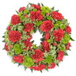 A full, circular wreath crafted for a funeral or memorial occasion is photographed against a stark white backdrop, making its deep red and lime green tones stand out in sharp relief. The design is rich and compact, with flowers and foliage tightly arranged so that the ring appears solid and complete. The primary blooms are red carnations, their characteristic ruffled petals forming dense, rounded flower heads that march evenly around the circle. The carnations vary subtly in size and openness, from small, half-open buds to wide, generous blooms, giving the wreath a natural, breathing quality. Interspersed among them, lime green button chrysanthemums are tucked in clusters, their tidy, globular shapes and tightly packed florets offering a crisp contrast to the softness of the carnations. The fresh green colour lightens the overall effect, suggesting the hope and renewal that can be felt even during times of loss. The flowers rest on a base of lush greenery composed of dark, feathery ferns and other mixed foliage, which add depth and shadow, making the blooms appear to float slightly above the greens. Variegated leaves with pale, creamy edges weave through the base, breaking up the darker tones and providing gentle visual movement, like glimpses of mixed hedging around homes close to Brent Cross. A looped ribbon in shades of green, subtly striped, is threaded into one side of the wreath, blending seamlessly with the foliage rather than demanding attention. The finished piece feels thoughtfully balanced and reverent, a fitting floral tribute for delivery to churches, crematorium chapels, or family homes in the Brent Cross area when words alone are not enough.