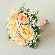 This bridal bouquet blends soft peach roses with a froth of white gypsophila to create a composition that feels both intimate and refined, captured here in gentle, natural light. The peach roses open with creamy centers and blushing edges, their petals layered like silk; between them, delicate baby's breath forms a diaphanous cloud that lifts the arrangement and adds a note of innocence. Glossy emerald foliage frames the flowers, giving structure and a cool visual counterpoint to the warm peach tones. The stems are bound by a smooth peach satin ribbon, finished with a row of pearls threaded along its edge, a subtle nod to heirloom traditions and quiet elegance. When held, the bouquet would settle comfortably in the hand - light, fragrant with a discreet rose scent, and reassuringly balanced. As someone who arranges wedding flowers for neighbourhood couples around Brent Cross and the High Road into Cricklewood, I craft pieces that complement local venues and church ceremonies; this style sits beautifully alongside afternoon receptions near the shopping centre or intimate vows in a garden close to Hendon. Created with attention to proportion and texture, this bouquet by Brent Cross Flowers evokes tender confidence and a calm joy - a keepsake-ready design that honors the moment with gentle colour, graceful form, and a careful hand.