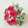 A round, carefully constructed bouquet of red roses and white baby's breath lies on a pale, linen-like surface, styled as though a florist near Brent Cross had just finished tying the final ribbon before a wedding. Central to the composition are six or seven rich crimson roses, their heads full and open, petals densely layered and curling outward in elegant spirals. The velvety texture of the roses is almost visible to the touch, suggesting the soft, warm fragrance that often fills a room when fresh blooms arrive. Nestled in and around these roses are generous sprays of gypsophila, or baby's breath, their tiny white flowers forming frothy, cloud-like clusters. The contrast between the bold red and the delicate white creates a balance of passion and gentleness, like a visual echo of vows spoken in a quiet ceremony near Brent Cross station. Around the edges, deep green foliage provides a natural frame, the leaves broad and slightly glossy, adding depth and supporting the flowers without stealing focus. The stems are aligned and bound into a comfortable handle wrapped in red ribbon, which is embellished with a neat pattern of pearl-style beads or dots that swirl or stripe down the length, giving the bouquet a polished and ceremonial look. The off-white background fabric gently cradles the bouquet, its subtle texture adding warmth while ensuring the colours remain the centre of attention. This arrangement, with its timeless combination of red roses and baby's breath, feels ideal for weddings, anniversaries or romantic deliveries across Brent Cross, from homes along the A41 to intimate gatherings near the shopping centre and local hotels.