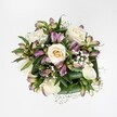 An overhead view reveals a compact, hand-tied bouquet laid on a clean, brilliant white background, every detail of the flowers standing out as if lit by soft studio light. At the heart of the arrangement, creamy white and pale ivory roses bloom at different stages: some tight buds cradle a hint of buttery yellow at their centres, while others are fully opened, their velvety petals spiralling outwards in generous layers. Threaded between the roses are elegant stems of alstroemeria, or Peruvian lilies, their slender buds and partially open flowers bringing a gentle play of movement. Their petals show a blend of mauve, lavender, and pink, with fine streaks of green and deeper berry tones, like the last colours of an evening sky over nearby Brent Cross and Hendon Way. Wisps of baby's breath create tiny constellations of white, each cloud-like cluster softening the spaces between the larger blooms and lending the bouquet an airy, romantic halo. Rich, deep green foliage forms a structured base, the broad glossy leaves cupping the flowers and framing them with calm assurance, suggesting freshness as if just trimmed in a local Brent Cross florist's workshop. The composition feels both refined and welcoming, ideal for a birthday, an anniversary, or a quiet thank-you. Although no vase is visible, the tight, rounded shape suggests it could be easily cradled in two hands, ready for same-day delivery to homes and offices around Brent Cross Shopping Centre, Golders Green, or Cricklewood, carrying with it a sense of thoughtful care and gentle celebration.