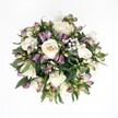 Top-down view of a hand-tied, circular bouquet laid against a crisp, pure white background, the clean space around it making every flower and leaf stand out in sharp relief. At the heart of the arrangement are velvety cream and soft ivory roses, some fully open in perfect spirals, others just beginning to unfurl, their petals catching the light with a gentle satin sheen. Tucked closely among them are clusters of deep lavender and rich purple alstroemeria buds, their outer petals still mostly closed, tipped with fresh green at the base so they look poised to open later in the day. Between these main blooms float delicate clouds of white baby's breath, each tiny flower forming a light, airy mist that softens the contrast between purple and cream. Around the edge, glossy dark green foliage fans out in a natural halo, the leaves slightly curved and layered to give depth and fullness without overpowering the central roses. The lighting is soft and even, as if the bouquet were placed near a bright window in a Brent Cross townhouse, minimizing shadows and emphasizing the freshness of every petal and leaf. The overall feeling is serene and romantic, a quietly luxurious bouquet well-suited to an intimate anniversary dinner at home, a thoughtful sympathy gesture, or a refined bridal posy. The composition, with its modern overhead perspective and white backdrop, feels contemporary yet timeless, the kind of classic rose and alstroemeria design you might order for same-day delivery to a friend near Brent Cross Shopping Centre or along the tree-lined streets leading towards Hendon and Golders Green.