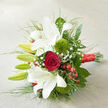 The photograph shows an artfully arranged bouquet placed on a softly woven, off-white surface, angled as though just set down on a table in a Brent Cross home before being handed to its recipient. Dominating the design, white oriental lilies open grandly, their wide, star-like petals slightly ruffled at the tips and dusted near the centres with subtle reddish speckles that draw the eye inward. Several elongated green buds rise above and between the open blooms, still tightly closed, bringing a sense of rhythm and future blossoming to the composition. At the centre, a single, rich red rose blooms in a perfect spiral, its velvety petals layered closely together in a classic symbol of romance-equally fitting for proposals, anniversaries, or wedding celebrations in venues around Hendon Way. Adding a striking textural counterpoint, two round 'Green Trick' dianthus nestle amongst the lilies, their vivid, moss-like fuzziness creating lively contrast against the smooth, satiny petals. Fine sprays of gypsophila thread delicately throughout the bouquet, each tiny white flower like a star in a light haze, softening the overall effect. Near the base, clusters of glossy red hypericum berries echo the tone of the central rose, their polished surfaces catching the light and hinting at winter festivities or intimate holiday gatherings. A generous collar of greenery frames the flowers, with deep green leaves and feathery, grass-like stems adding both depth and movement. The stems are expertly gathered and wrapped in a wide, red satin ribbon that gleams softly, its tied end resting toward the bottom right of the frame. The bouquet feels both timeless and contemporary, perfectly suited for same-day delivery around Brent Cross to mark moments of love, gratitude, or celebration.