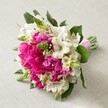 Set against a soft, sand-hued surface, this vibrant bouquet shines with Brent Cross flair-a harmonious blend of large, hot pink peonies bursting with ruffled petals, their color evoking festive energy reminiscent of weddings at Brent Cross Park. Soft, white Alstroemeria adorned with subtle maroon streaks weave their way through the arrangement, lending a graceful lift and refined balance. Sprigs of lively green, perhaps Veronica or nascent Hyacinth, create dynamic texture and an infusion of natural freshness, reminiscent of early spring mornings along Tilling Road. Clusters of small, creamy, bell-shaped flowers are gently scattered, softening the bouquet's bold tones and imparting a whimsical, romantic touch. Tucked between every bloom, rich green foliage adds depth, anchoring the vivid palette and rounding out the organic shape. The stems are skillfully bound with a gleaming pink satin ribbon, giving the bouquet its finished, elegant presence-ideal for a bride, wedding celebration, or special local event. Radiant in natural light, this composition captures the timeless beauty, joyful mood, and heartfelt celebration that defines Brent Cross Flowers' approach to bespoke arrangements.
