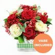 A beautifully composed rose arrangement stands out crisply against a white background, its red and white tones creating a romantic focal point that would complement any Brent Cross living room or office. The eye is first drawn to the large, velvety deep red roses, each bloom fully open, with petals curling and overlapping like soft fabric. Nestled among them are creamy white roses, equally full and unfurled, whose gentle brightness softens the intensity of the red, resulting in a harmonious, elegant contrast. Between these main blooms, a fine haze of tiny bright red filler flowers-evoking dyed gypsophila-adds a light, airy layer, as though a delicate red mist has settled over the petals. Dotted throughout, glossy red hypericum berries sit like tiny round ornaments, adding structure, texture, and a festive touch that would suit intimate dinners or celebratory gatherings near Brent Cross Shopping Centre. Framing the roses is a selection of fresh greenery: elongated eucalyptus sprigs with their cool, muted tones and other foliage in rich greens. These leaves introduce varied shapes and subtle movement, helping the bouquet feel organic and three-dimensional rather than rigid. The flowers rise from a clear rectangular glass vase, whose transparent sides reveal the neatly cut stems arranged in clean, parallel lines, a quiet testament to expert floristry. Around the middle of the vase, a green and white gingham ribbon is wrapped securely, bringing a charming rustic note that recalls relaxed family kitchens in nearby Hendon or Golders Green. In the lower right corner of the overall image, an orange circular graphic with bold white text reads VASE INCLUDED, clearly indicating that this is a complete, ready-to-enjoy floral gift-perfect for anniversaries, Valentine's surprises, birthdays, or simply sending a warm message of affection across the Brent Cross area.