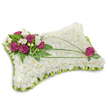 A carefully shaped, rectangular pillow of pristine white chrysanthemum blooms rests against a clean white backdrop, the dense cushion of small florets giving a soft, cloudlike texture that invites a gentle touch. The floral surface reads as a quiet field of white: tiny petals layered tightly to create a plush, peaceful plane that absorbs light and radiates calm. Around the outer edge a narrow band of fresh lime-green foliage and tiny green buds subtly defines the silhouette, adding a crisp, natural frame to the composition. In the upper left corner a rich cluster of deep magenta roses provides the arrangement's emotional focal point-velvety petals unfurling in generous spirals, balanced by little white accent blooms and glossy, mid-green leaves that lend depth and life. From the upper right down toward the middle left, two or three long, slender blades of green-likely bear grass or lily grass-sweep across the white chrysanthemum field in a graceful diagonal, introducing movement and drawing the eye across the tribute. A single magenta rose, echoing the main cluster, is placed near the upper right for visual balance, nestled among a few darker green leaves. The outer lime ribbon trim is folded into a soft pleat, creating a neat, slightly ruffled border that completes the pillow's silhouette. Soft studio lighting casts a faint shadow beneath the cushion, giving the piece modest volume while keeping the focus on its serene white surface and the warm, consoling pop of magenta. This traditional sympathy cushion, mindful and restrained, is the kind of floral tribute chosen to express heartfelt condolences and to offer quiet comfort at a funeral or memorial in the Brent Cross area, near local chapels and parks.