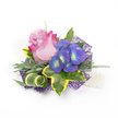 Pinned on a clean white background, this compact corsage reads as a small, handcrafted celebration: a single partially open rose takes centre stage, its velvety petals shading from a pale lavender-pink at the heart to a lively fuchsia at the edges, suggesting both intimacy and exuberance. Beside it, a tight cluster of indigo-purple florets - reminiscent of garden hydrangea or small ornamental orchids - catches the eye with tiny bright blue and lime-yellow centres that seem to glow against the deeper purple. The blooms are cushioned by a tapestry of foliage: broad, variegated ivy leaves with deep emerald centres and sunlit yellow rims create a bold, classic frame; soft, silvery-green foliage, like lavender or dusty miller, introduces a muted, powdery texture; and a slender, striped green-and-cream leaf is artfully curled to add architectural movement. Fine asparagus-like sprigs filter through the composition, lending an airy, feathery softness that balances the richer petals. Underneath, a layer of intricate, web-like dark purple mesh peeks out, lending depth and a contemporary shimmer, while a short strand of lustrous white pearls at the lower right reads as a wristlet or delicate lapel accent. The lighting is soft and even, emphasising the tactile contrast between plush blooms and crisp greenery. As a local florist might say, this piece is tailored for momentous days - weddings, proms, or anniversaries - and feels right for a Brent Cross celebration, whether it's pinned on a lapel near the shopping centre or carried through quieter streets toward a family gathering. It's small in scale but rich in texture and sentiment, made to be seen, touched, and remembered.