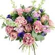 Against a flawless white background, this hand-tied bouquet seems to hover in the frame, its colours and textures carefully balanced like a thoughtfully curated piece in a Brent Cross boutique. The central roses, lush garden varieties in blush pink, dusty mauve, and antique rose, open in layered spirals that give the impression of softness and depth, every petal slightly cupped as if holding the light. Among them, generous carnations add playful movement; their ruffled petals are shaded from creamy beige and pale blush at the centre to richer rose and plum tones along the fringes, creating an almost painterly transition of colour that invites you to look closely. Deep indigo-blue bloom spikes, with buds shaped much like sleek tulips, punctuate the arrangement, their cool intensity enhanced by a striking royal blue anemone placed near the lower front. This anemone, with its velvety petals and dark centre, acts as a visual anchor in the sea of softer hues. Traveling upward through the bouquet, slender stems of stock in lilac and pale lavender carry small, multi-petalled flowers that introduce height and a gentle, ethereal quality, reminiscent of the first soft blossoms of early spring. All of this colour rests upon an abundant base of foliage: rounded, silvery eucalyptus leaves mingling with faces of deeper green, creating a full, natural collar around the blooms. At the bottom, the stems are neatly gathered and tied, showing the care of an experienced florist's hand. This is the kind of bouquet you might send across Brent Cross to celebrate a birthday, mark a new home, or offer a heartfelt thank-you, bringing refined colour and quiet joy into someone's day.
