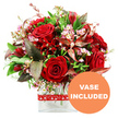 A visually striking bouquet of red roses and complementary blooms is set against a clean white background, styled in a modern glass vase that could easily sit on a dining table in Brent Cross after a same-day delivery. The arrangement centres on velvety red roses, their petals rich and saturated, some rosebuds still wrapped tightly while others have opened generously to reveal intricate layers that speak of affection and romance. Around them, clusters of deep crimson flowers, much like alstroemeria or similar multi-petalled stems, create sculptural shapes and add volume, filling the design with texture and a sense of movement. Interlaced between these larger flowers are stems of tiny, pale pink and white blossoms-likely waxflower or limonium-whose miniature flowers gather in airy sprays that gently soften the bold reds and contribute a delicate, almost frothy detail. Lush greenery forms a graceful collar around the bouquet, mixing broader, darker leaves with fine, lighter sprigs to sculpt a rounded, hand-tied look that feels both full and harmonious. Tucked among the greens are distinctive burgundy and reddish-brown leaves, some with faint veining, which provide a subtle yet impactful contrast, echoing the passion of the roses while adding refined drama. The blooms are anchored in a sleek rectangular glass vase, its transparent sides allowing the stems and crystal-clear water to be seen, reflecting professional conditioning and an eye for modern design. A red ribbon, decorated with small white hearts, is tied around the vase, reinforcing the romantic message and making the arrangement an ideal choice for anniversaries, Valentine's Day, or just-because declarations of love around Brent Cross, Hendon, and nearby Temple Fortune. In the bottom right corner, a circular orange badge with crisp white uppercase text reads VASE INCLUDED, clearly indicating this bouquet is delivered complete and ready to enjoy without the need for an extra container.