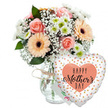 This carefully arranged Mother's Day gift set is shown against a clean white background, its colours and shapes standing out with clarity, much like a display in the quiet morning light of a Brent Cross florist's window. In the centre left of the frame is a clear, subtly patterned glass vase filled with water and sturdy green stems. Around the neck, a slim piece of natural twine is tied into a modest bow, a small rustic detail that adds character and a sense of personal touch. The vase holds a generous, dome-shaped bouquet in soft, comforting tones. Peach-pink roses, some fully open and others just beginning to unfurl, create a focal point, their spiralling petals plush and velvety. Interspersed among them are several peach gerbera daisies, their many narrow petals fanning out evenly around deep brown or black centres that add a strong visual contrast. Floating between these larger blooms, clusters of delicate white baby's breath add an airy, mist-like texture that softens the composition. Compact white chrysanthemums with pale green centres tuck into the gaps, boosting fullness and bringing a crisp freshness, as if the flowers had just arrived from an early-morning market. The bouquet is framed by lush green foliage, the leaves of different shapes and sizes giving the arrangement depth and a natural, garden-cut feeling that would suit any home around Brent Cross. To the right of the vase, gently leaning forward, is a heart-shaped Mylar balloon tethered to the arrangement. Its surface is a bright, clean white scattered with small metallic gold and silver dots that evoke celebratory confetti. In the middle of the balloon sits a peach-coloured heart containing the message HAPPY Mother's DAY in bold black lettering, with the word Mother's written in an elegant, flowing script. Behind the flowers, almost hidden, the corner of a white greeting card peeks out, suggesting a handwritten note. Altogether, the bouquet, card, and balloon form a tender, joyful tribute, perfect for a Mother's Day delivery across the Brent Cross area.