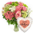 A bright, affectionate Mother's Day gift duo is presented against a smooth white background: a generous floral arrangement in a clear glass vase paired with a gleaming heart-shaped balloon. The bouquet forms a rounded, almost cloud-like shape of colour, dominated by pinks, corals, fresh greens and soft whites that call to mind the first warm days of spring in Brent Cross. At the centre, several open pink roses reveal layered petals with slightly darker edges, giving them a soft, romantic depth. Wrapped around these focal blooms, clusters of coral-pink flowers, similar to kalanchoe in their dense, starry look, mingle with smaller spiky coral blossoms, adding playful texture and a sense of movement. Lime-green button chrysanthemums and frilly chartreuse, cockscomb-style elements stand out with their vibrant hue and intriguing, almost velvety texture, providing a modern counterpoint to the classic roses. White spray chrysanthemums, with clean, daisy-like faces, are woven throughout the design, catching the light and keeping the palette crisp. Tiny pale-tipped chrysanthemum centres and dark green leaves help build subtle layers of detail, giving the arrangement an expertly crafted feel that suggests the skill of a local Brent Cross florist. The clear vase at the base reveals orderly stems and water, grounding the design. To the right, a shiny foil heart balloon tilts invitingly toward the bouquet. Its white or pale silver surface is scattered with irregular dots of gold, silver and soft peach, and in the middle a warm coral heart frames the greeting HAPPY Mother's DAY in stylish black type. Together, the flowers and balloon create a complete, joy-filled presentation, ideal for marking Mother's Day with love and appreciation anywhere around Brent Cross.